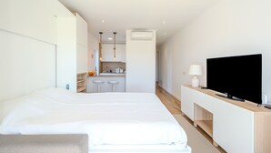 Una habitación de hotel moderna con una cama grande, televisor, una kitchenette pequeña y un baño.