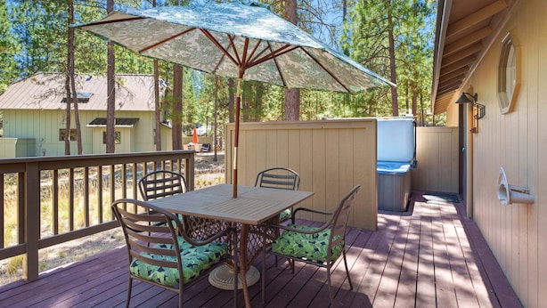 Una terraza de madera con una mesa, sillas, una sombrilla y un jacuzzi.