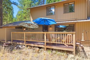 A wooden deck with a railing, a blue umbrella, and a wooden bench.