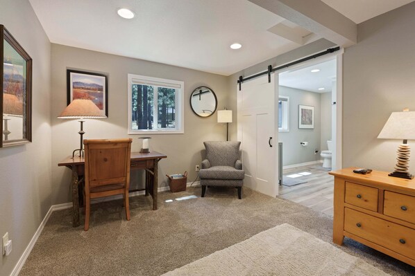 A room with a desk, chair, lamp, and a view of a forest through a window. - 8 East Butte - Heart of Sunriver, Game Room, Hot Tub, Bikes, SHARC, A/C (Bend)