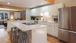 Una cocina moderna con una isla central, taburetes de bar, un refrigerador de acero inoxidable y piso de madera.