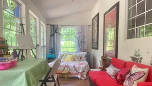 Ein gemütliches Zimmer mit einem Bett, einem roten Sofa, einem Schreibtisch mit Stuhl und großen Fenstern.