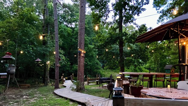 Eine Holzterrasse mit einer rustikalen Sitzgruppe im Freien, umgeben von Bäumen und Lichterketten.