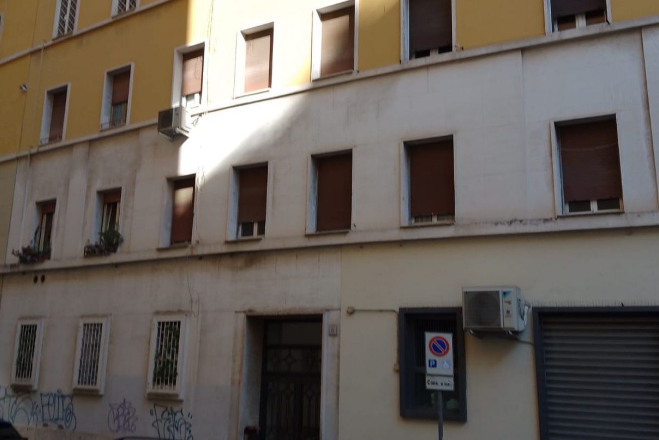 A multi-story building with several windows, some with shutters, and a no parking sign.