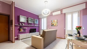 Una sala de estar moderna con un sofá, una mesa de comedor con sillas, un televisor y un cuadro en la pared.