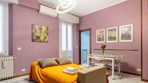 Un dormitorio con una cama, un escritorio y una silla, una ventana y una puerta.
