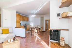 A living room with a sofa, a coffee table with cups, a kitchen area with wooden cabinets, a dining table with chairs, and a fireplace.