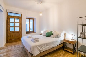 Une chambre à coucher avec un lit en bois, une table de chevet, une lampe, un plancher en bois, une porte et une fenêtre.