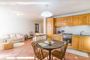 Un salon chaleureux avec une table ronde en bois, des chaises, un canapé et une cuisine dotée de meubles en bois et d’une cuisinière.