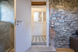 A doorway leading to a room with a tiled floor, a stone wall, and a wooden beam ceiling.