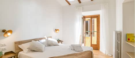A bedroom with a wooden bed, bedside lamps, a radiator, and a view of the outside.