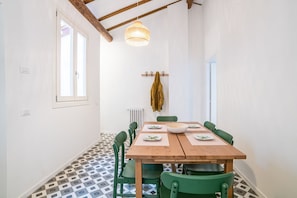 Zona pranzo con tavolo in legno, sedie verdi, lampadario e appendiabiti con giacca.