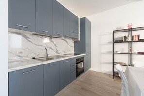 A modern kitchen with grey cabinets, a marble countertop, a built-in oven, and a black bookshelf. - GuestHost - Bright Apartment Affori, Milan (Milano)