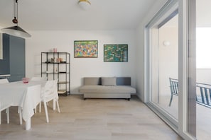 A modern living room with a sofa, dining table, chairs, and artwork on the walls.