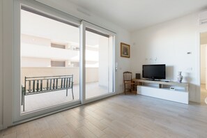 A spacious living room with a large sliding glass door leading to a balcony, a flat-screen TV on a wooden stand, and a white entertainment unit. - GuestHost - Bright Apartment Affori, Milan (Milano)
