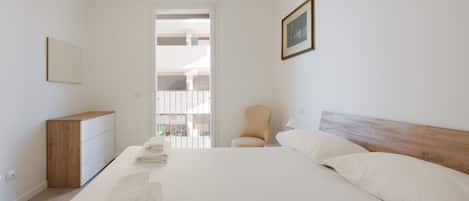 A bedroom with a bed, a chair, a dresser, and a door leading to another room.