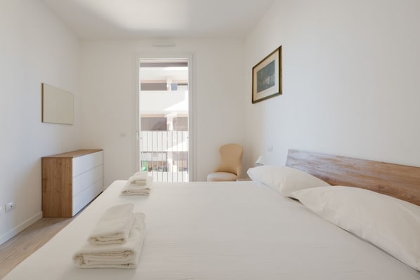 A bedroom with a bed, a chair, a dresser, and a door leading to another room.