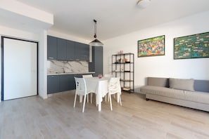 A modern kitchen with grey cabinets, a marble countertop, and a dining area with a white table and chairs. - GuestHost - Bright Apartment Affori, Milan (Milano)