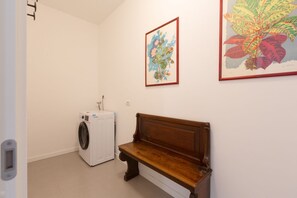 Une buanderie équipée d’un lave-linge, d’un banc et de deux illustrations botaniques encadrées accrochées au mur.