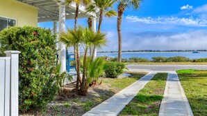 A coastal property with a paved driveway leading to a white building with a covered porch. Palm trees and shrubs are visible in the foreground. - The Dolphins of Salt Run (St. Augustine)