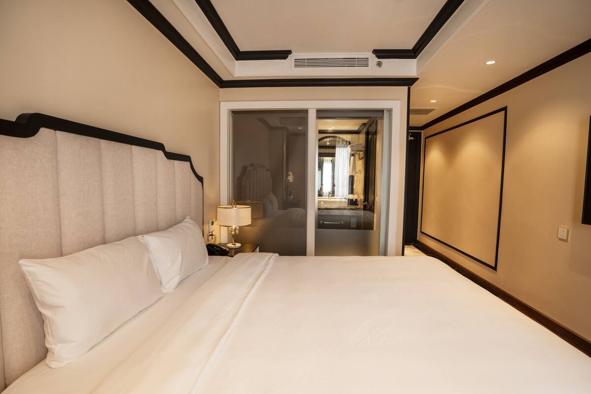 A hotel room with a large bed, a nightstand with a lamp, and a sliding door leading to a bathroom.