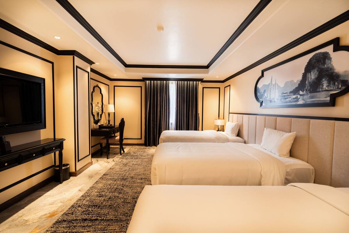 A hotel room with two beds, a flat-screen TV, a desk, and a large painting on the wall.