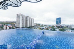 Une piscine à débordement située sur le toit, offrant une vue sur les gratte-ciel et un plan d’eau en arrière-plan.