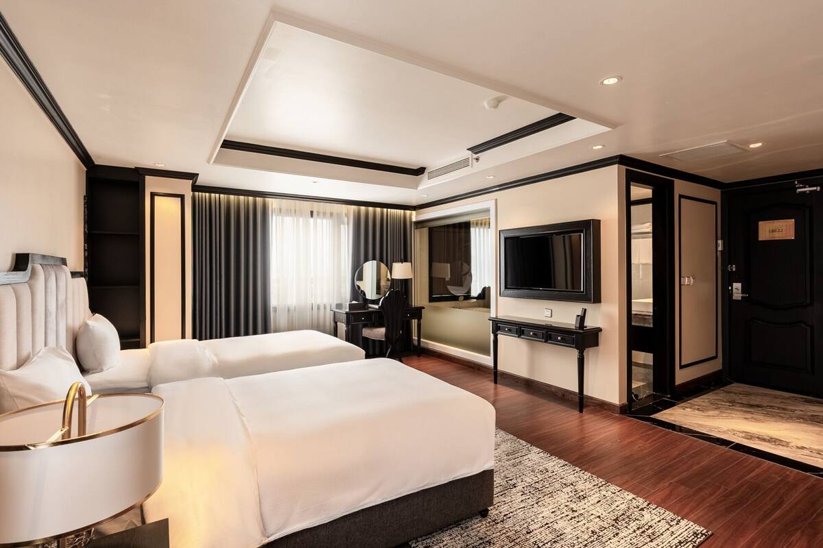 A modern hotel room with a large bed, a desk with a flat-screen TV, a mirror, and a wardrobe.