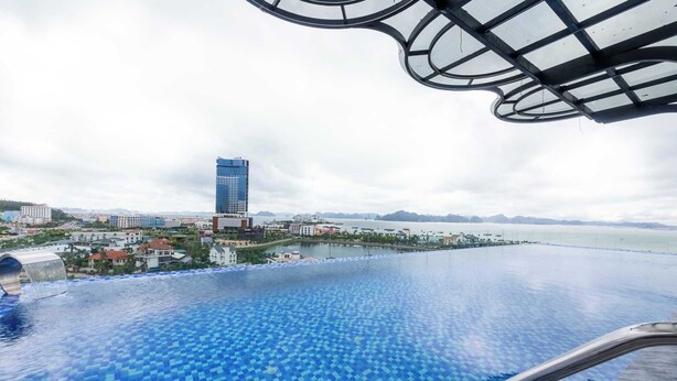 A pool with a checkered pattern, a view of a cityscape with buildings, and a body of water in the background. - FTE Ha Long Hotel (Bai Chay)