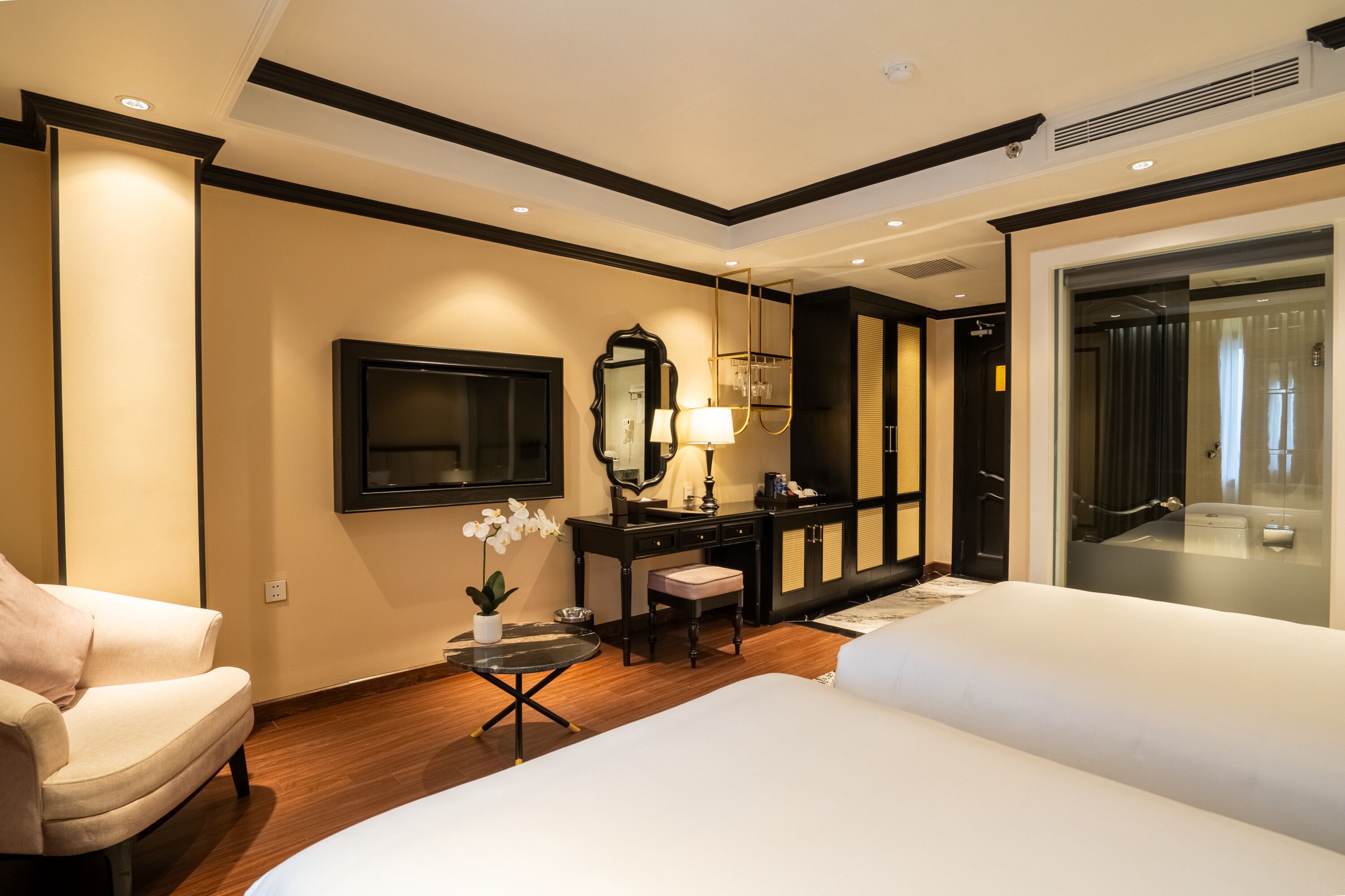 A hotel room with two beds, a desk with a lamp, a mirror, and a TV.