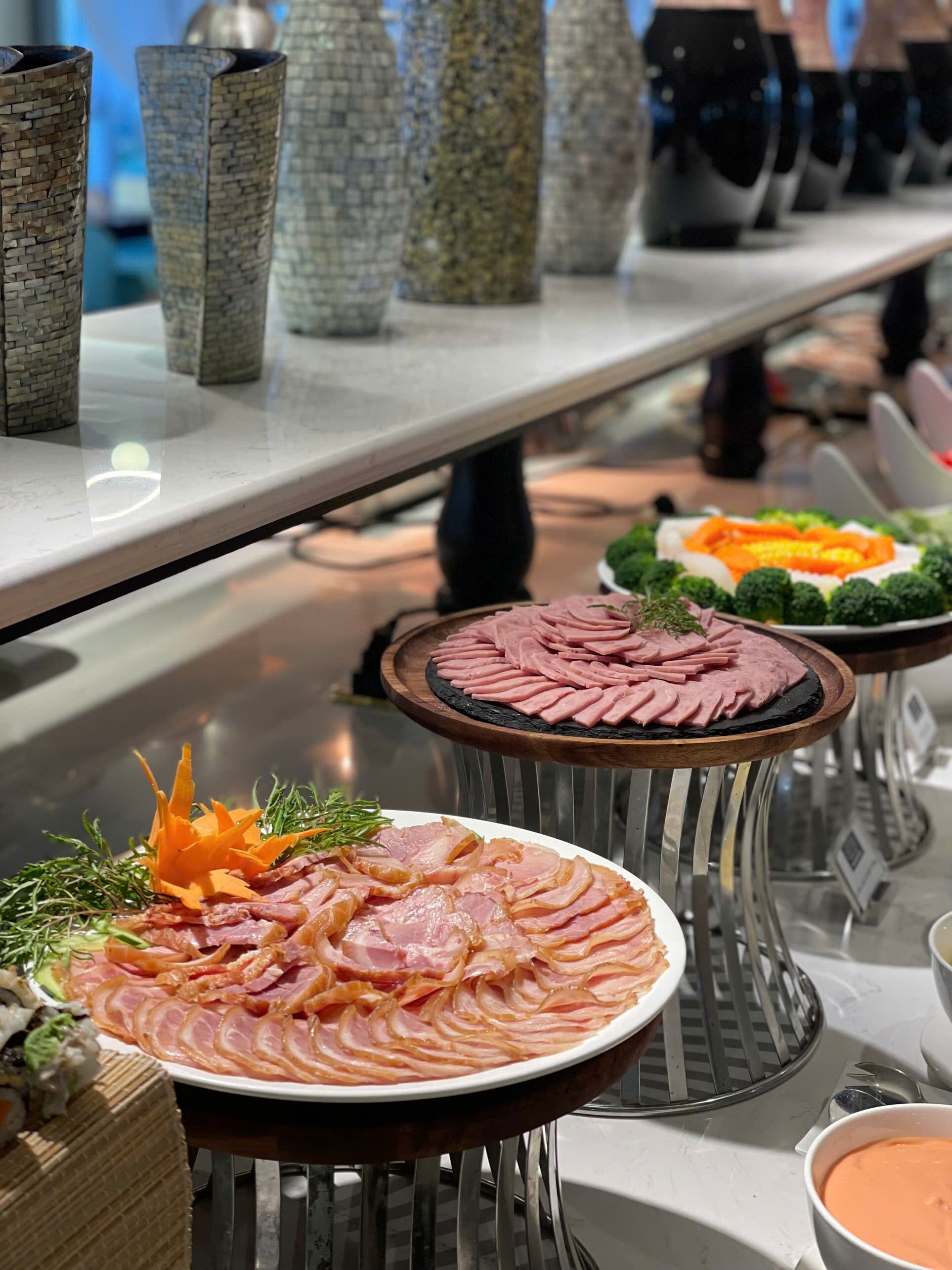 A buffet table with various food items including sliced meats, vegetables, and a bowl of soup.