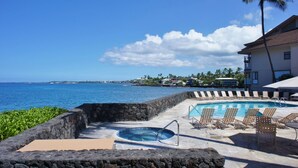 A pool area with lounge chairs and a view of the ocean. - Sea Village Oceanview Condo (Kailua-Kona)