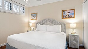 A bedroom with a large bed, two bedside tables with lamps, and two framed pictures on the wall. - Sea Village Oceanview Condo (Kailua-Kona)