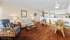 A living and dining area with a sofa, chairs, a coffee table, and a kitchen in the background. - Sea Village Oceanview Condo (Kailua-Kona)