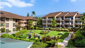 A hotel with multiple balconies, a well-maintained lawn, and outdoor seating areas. - Sea Village Oceanview Condo (Kailua-Kona)
