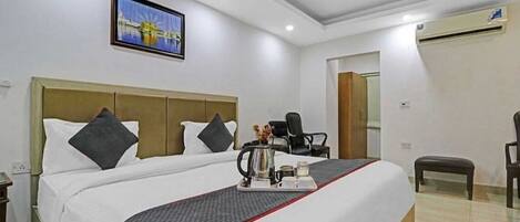 A hotel room with a large bed, a ceiling fan, an air conditioning unit, a framed picture on the wall, and a small table with a tray.