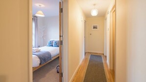 A narrow hallway with a bed on the left, a door at the end, and a small rug on the floor.