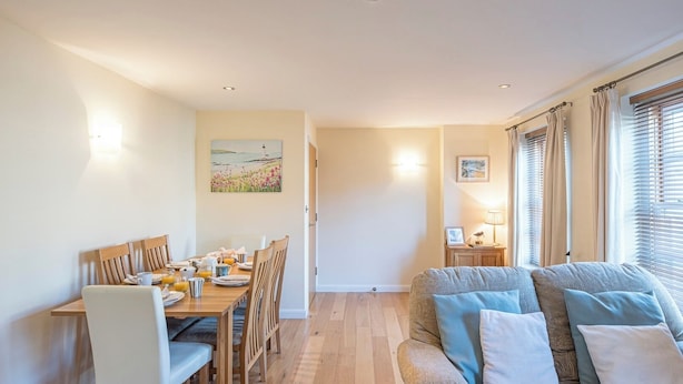 A cozy living room with a sofa, a dining table set for four, and a painting on the wall.