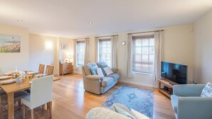 A spacious living room with a sofa, a TV, and a dining area with a table set for breakfast.