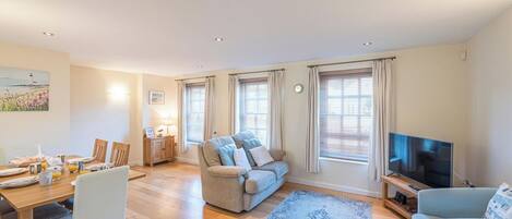 A spacious living room with a sofa, a TV, and a dining area with a table set for breakfast.