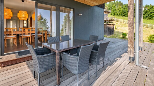 A covered outdoor dining area with a table and chairs, a wooden deck, and a view of the surrounding landscape. - Simonhöhe Kärntentraum EG by Interhome (Sankt Urban)