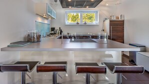 A modern kitchen with a central island, bar stools, a window with a view, and built-in appliances. - Simonhöhe Kärntentraum EG by Interhome (Sankt Urban)