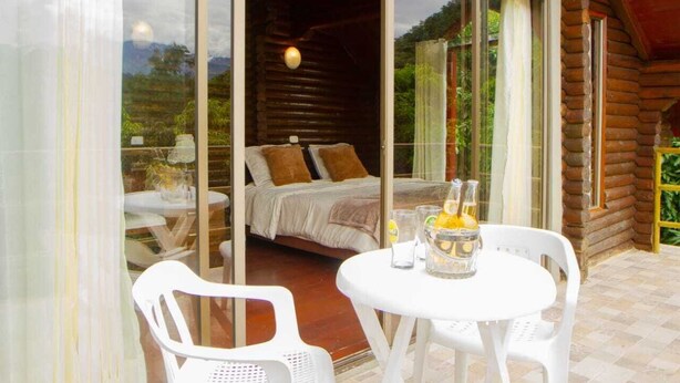 Une chambre confortable dans un chalet en rondins, avec un lit, une porte vitrée donnant sur l’extérieur, une table avec des chaises et une boisson.