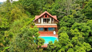 Une maison à deux étages avec une piscine, le tout entouré d’une végétation luxuriante.