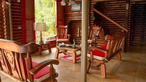 L’intérieur d’un chalet rustique en rondins de bois, avec des meubles en bois, une porte rouge et une vue sur la verdure à l’extérieur.