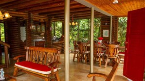 Une cabane rustique en bois, dotée d’un coin repas, de bancs en bois et d’une cuisine visible à travers les fenêtres.