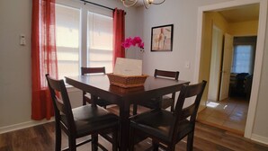Uma área de refeições com uma mesa e cadeiras de madeira, um cesto sobre a mesa e uma orquídea rosa.