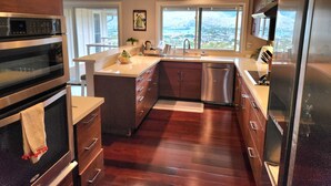 A modern kitchen with a large island, stainless steel appliances, and a view of a cityscape through the windows. - Amazing views! Exclusive & peaceful Hawaii Kai. Walk to ocean & hikes, Pool, AC, (Honolulu)