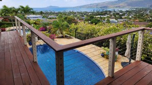 A wooden deck with a pool, surrounded by lush greenery and a view of a coastal town. - Amazing views! Exclusive & peaceful Hawaii Kai. Walk to ocean & hikes, Pool, AC, (Honolulu)