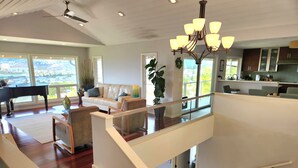 A spacious living area with a piano, a sofa, and a staircase leading to a balcony. - Amazing views! Exclusive & peaceful Hawaii Kai. Walk to ocean & hikes, Pool, AC, (Honolulu)